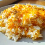 Close-up of a serving of fluffy white rice topped with melted, bright orange cheddar cheese, highlighting the cheesy rice texture.