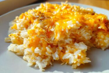Close-up of a serving of fluffy white rice topped with melted, bright orange cheddar cheese, highlighting the cheesy rice texture.