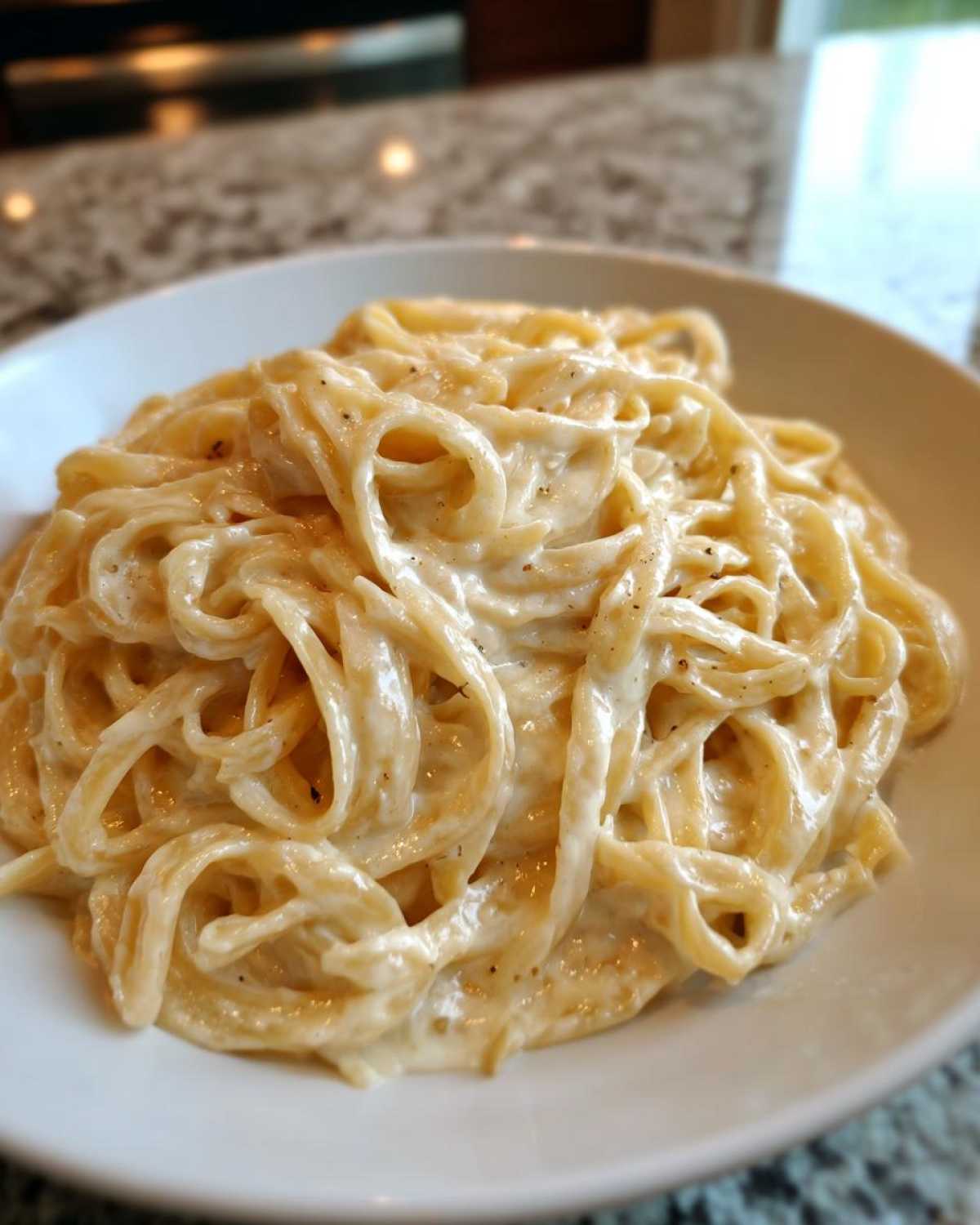 Close-up of fettuccine pasta generously coated in creamy Olive Garden Alfredo sauce, seasoned with pepper.