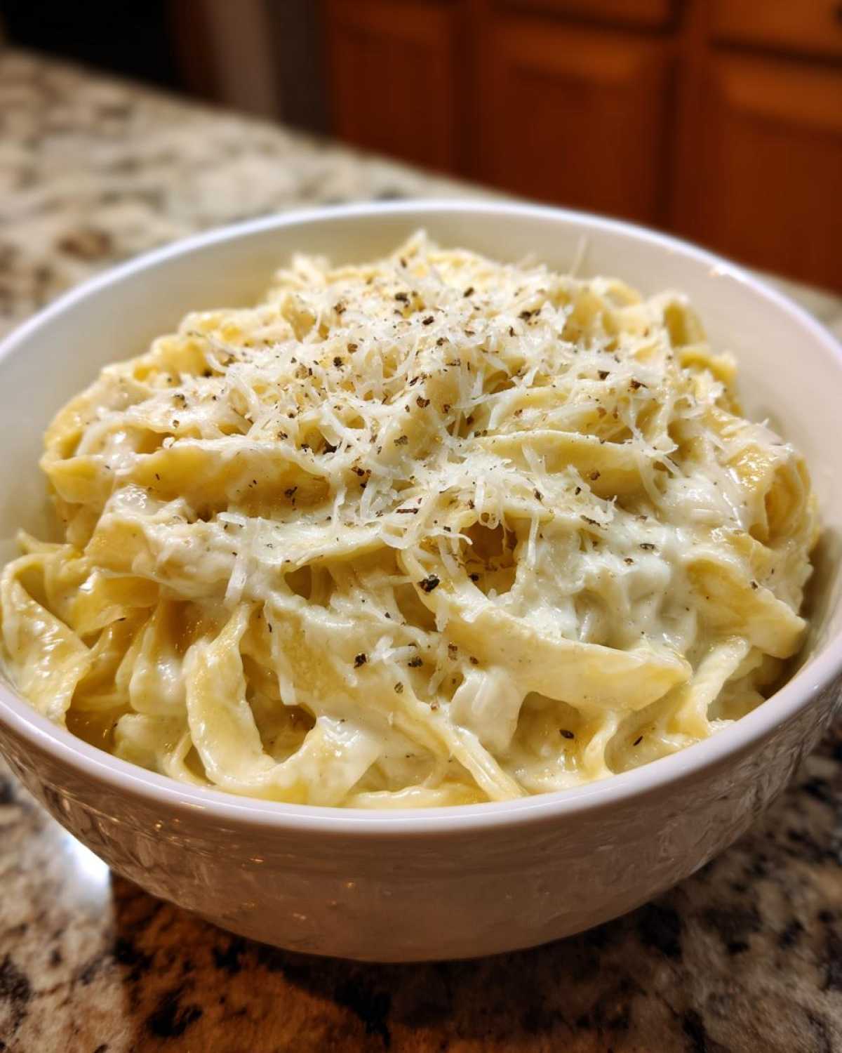 A close-up of fettuccine pasta coated in creamy homemade alfredo sauce and topped with grated Parmesan and black pepper.