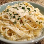 Close-up of fettuccine pasta coated in creamy homemade alfredo sauce, topped with grated Parmesan and parsley.