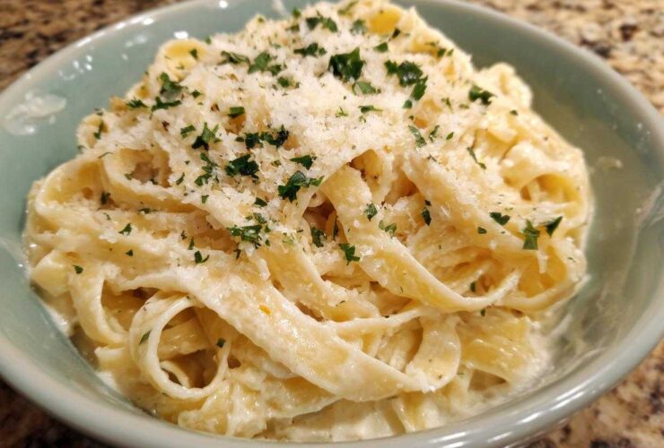 Close-up of fettuccine pasta coated in creamy homemade alfredo sauce, topped with grated Parmesan and parsley.