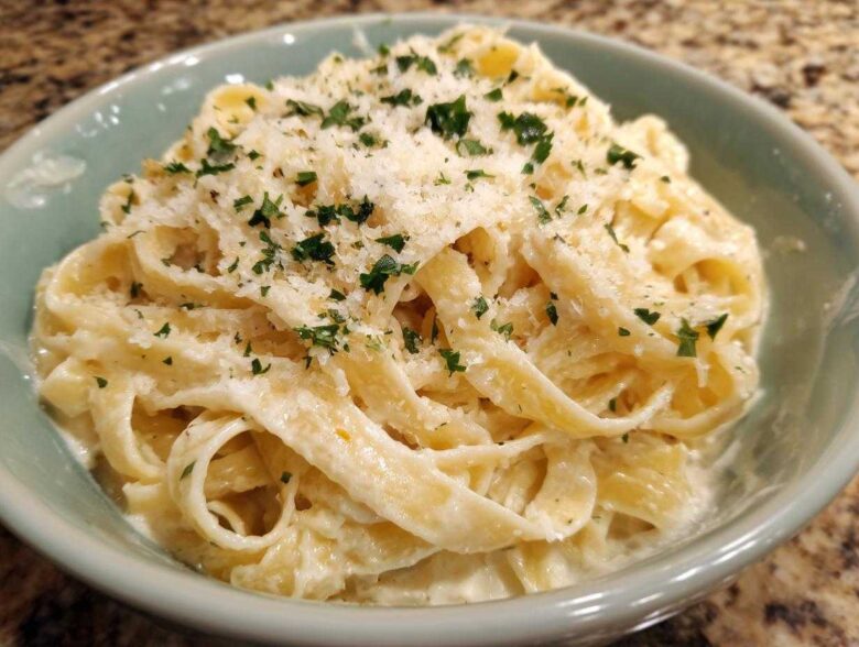 Close-up of fettuccine pasta coated in creamy homemade alfredo sauce, topped with grated Parmesan and parsley.