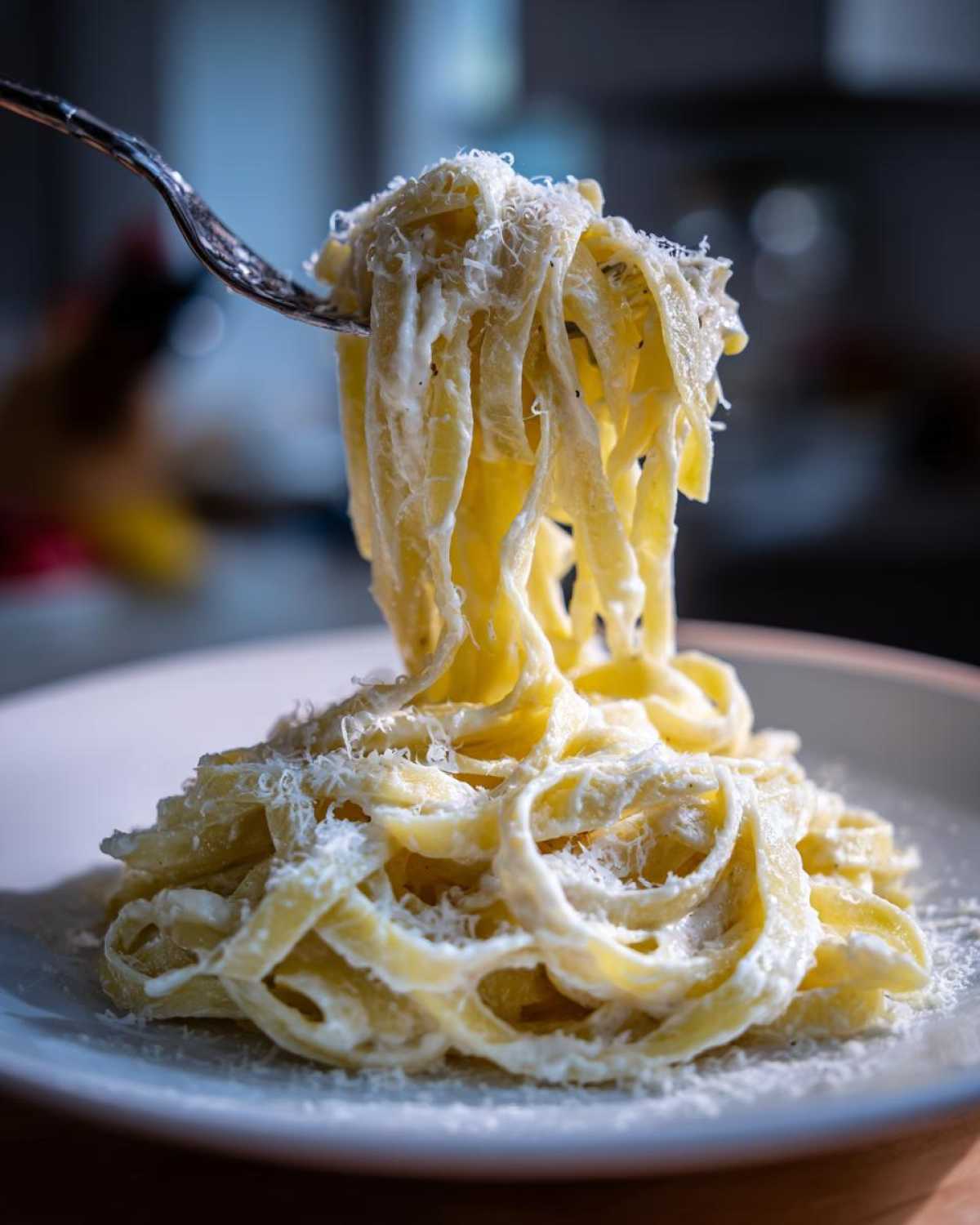 A fork lifting creamy fettuccine pasta coated in rich homemade alfredo sauce and topped with grated Parmesan cheese.
