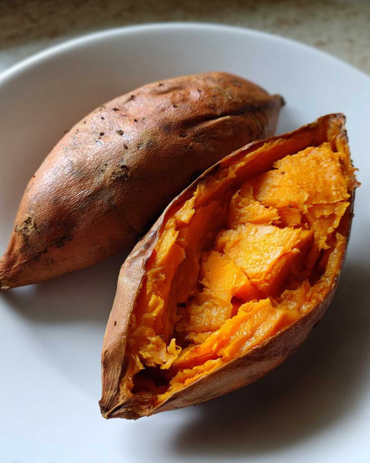 Close-up of a perfectly baked sweet potato split open, revealing its bright orange, fluffy interior.