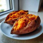 Two halves of fluffy baked sweet potatoes, seasoned and served on a white plate.