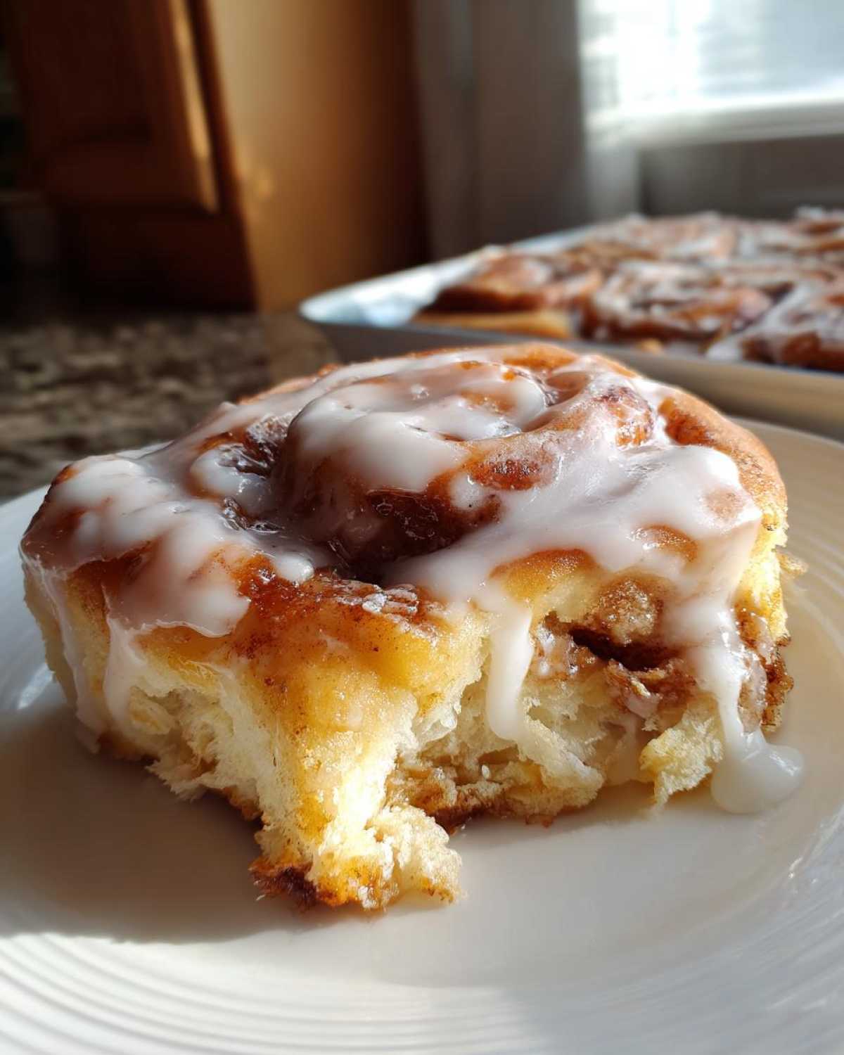 Close-up of a freshly baked cinnamon roll with thick white icing dripping down the sides, showing the fluffy interior.