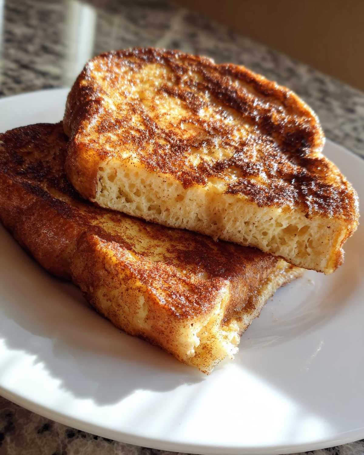Two thick slices of golden brown easy french toast dusted with cinnamon sugar, stacked on a white plate.