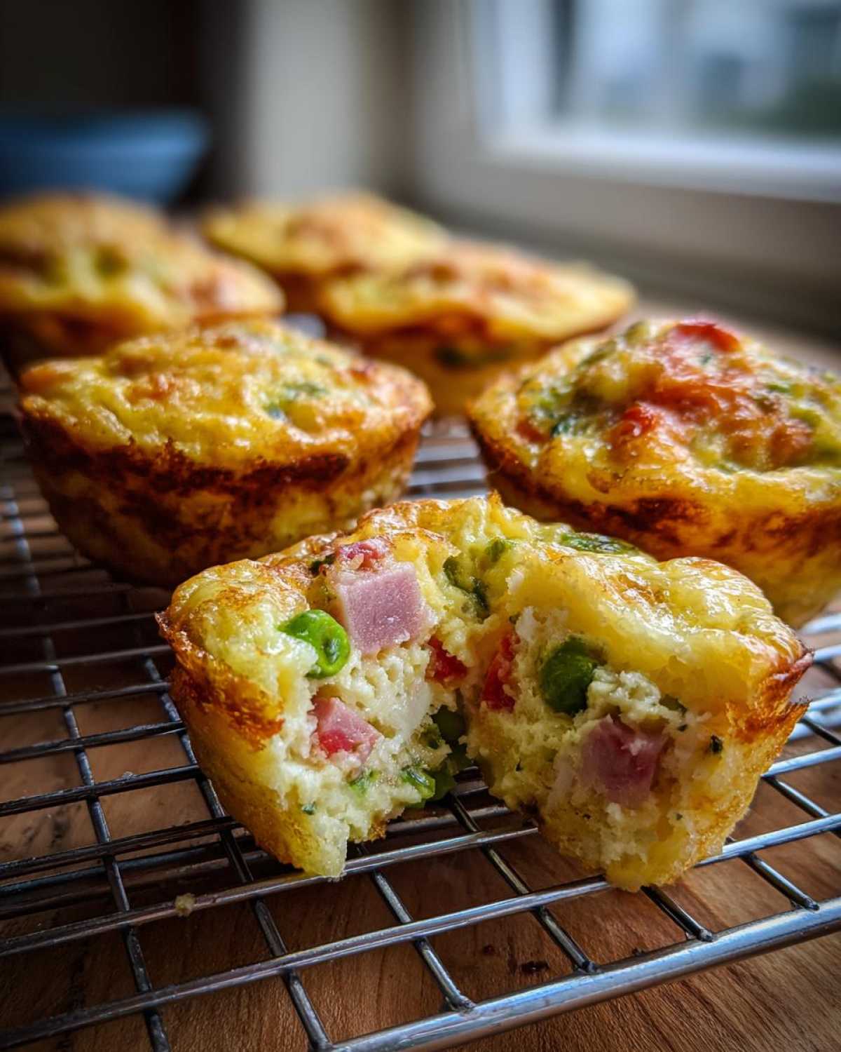 Close-up of a fluffy muffin tin egg bite cut in half, showing ham, peas, and egg filling.