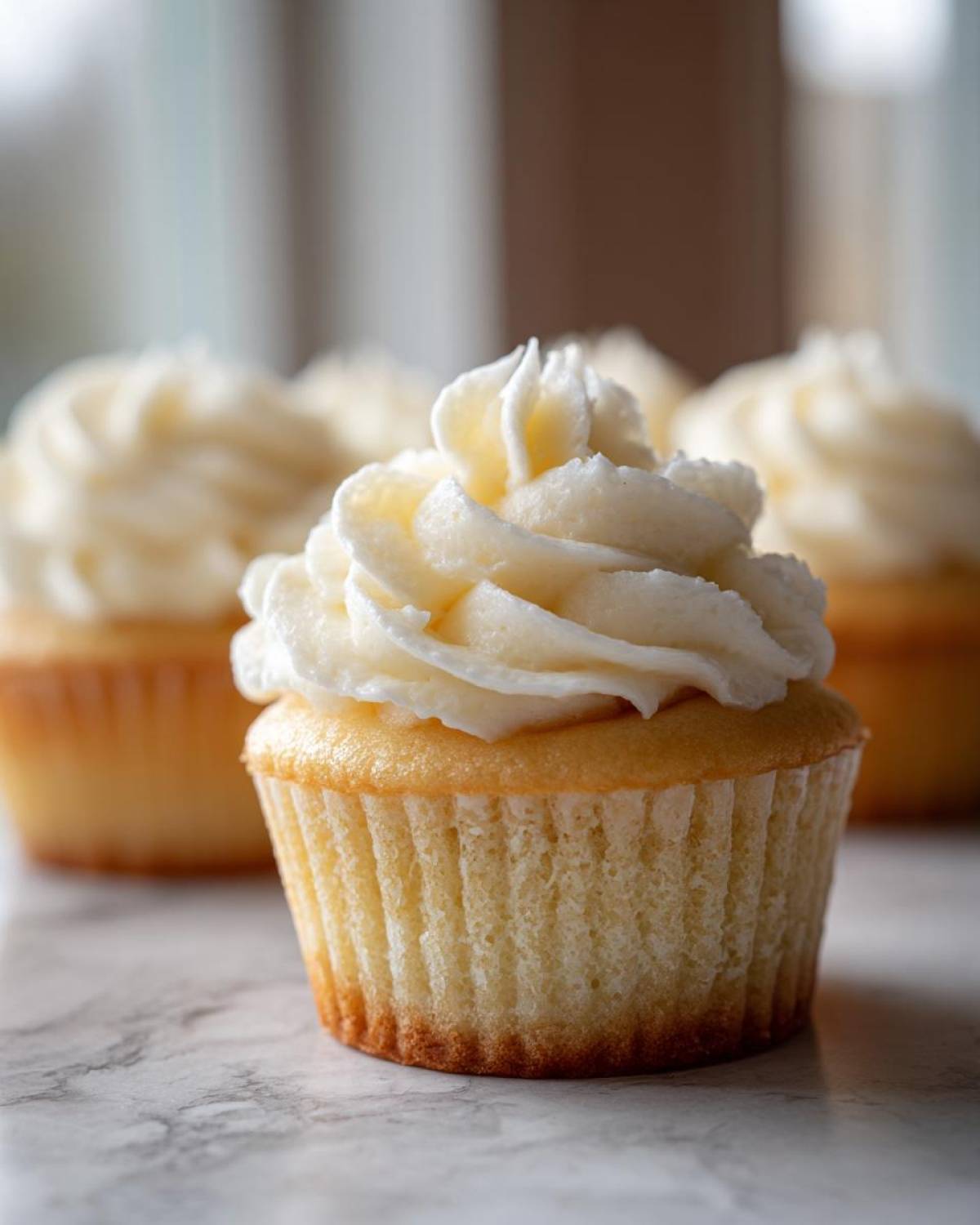 Close-up of a fluffy vanilla cupcake topped with a swirl of white vanilla buttercream frosting.