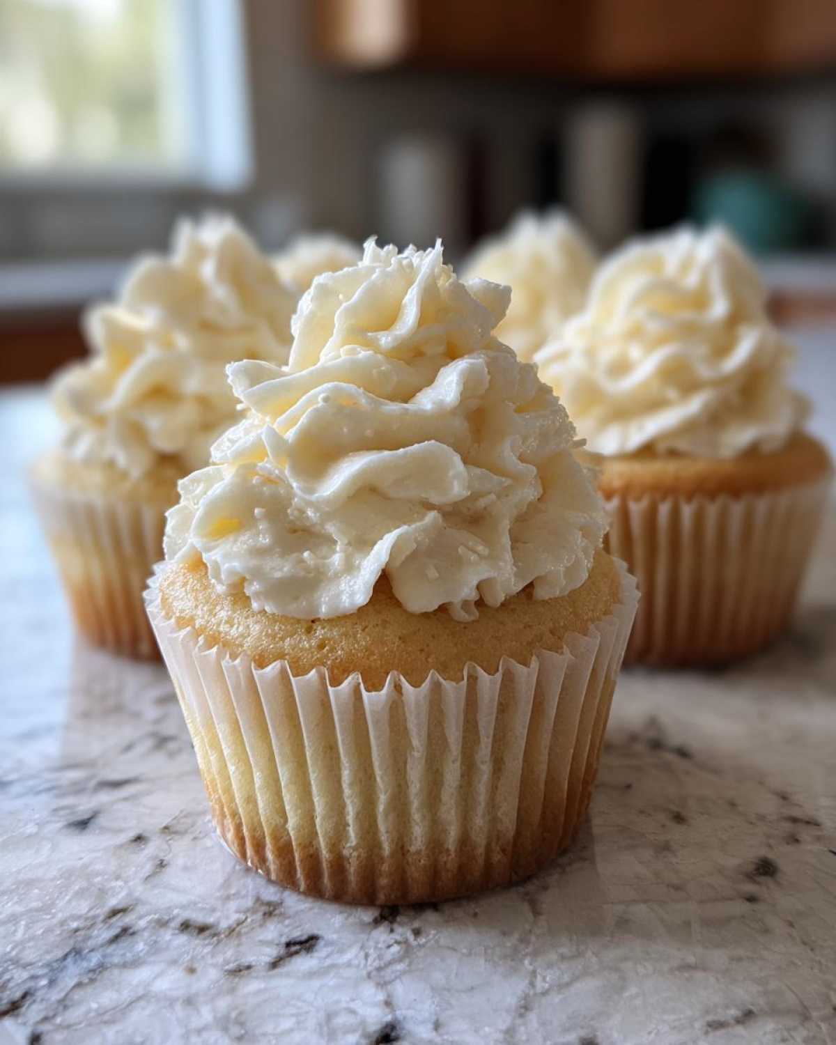 Close-up of a fluffy vanilla cupcake topped with generous swirls of white vanilla frosting.