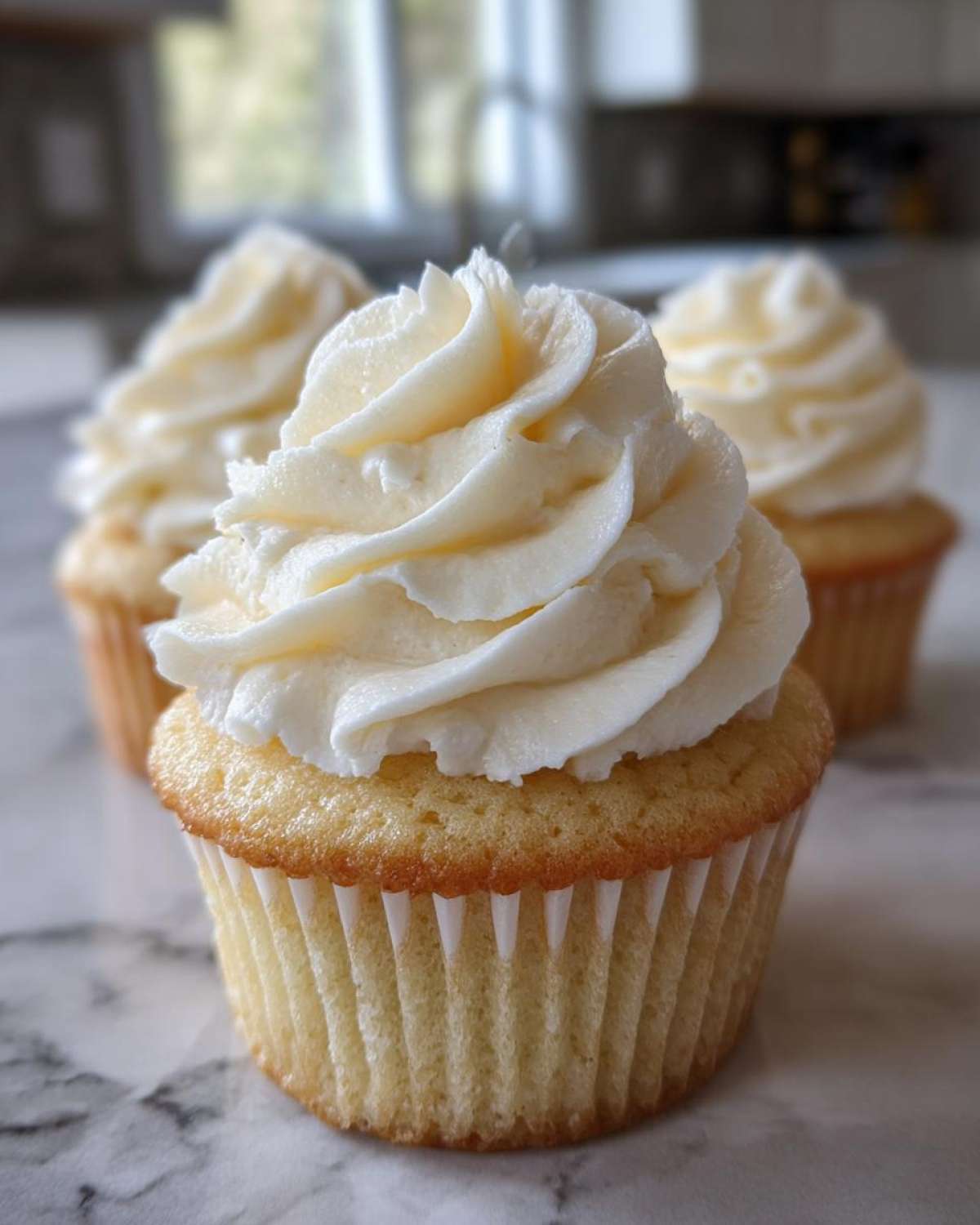 Close-up of a perfectly baked vanilla cupcake topped with a swirl of white vanilla buttercream frosting.