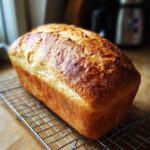 A golden-brown, perfectly baked loaf of whole wheat bread resting on a wire cooling rack.