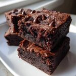 A stack of three rich, fudgy black bean brownies topped with chocolate chips on a white plate.