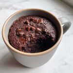 Close-up of a rich, fudgy chocolate mug cake topped with melted chocolate chips, ready to eat.