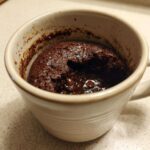 Close-up of a rich, fudgy chocolate mug cake with melted chocolate chips inside, ready to eat.
