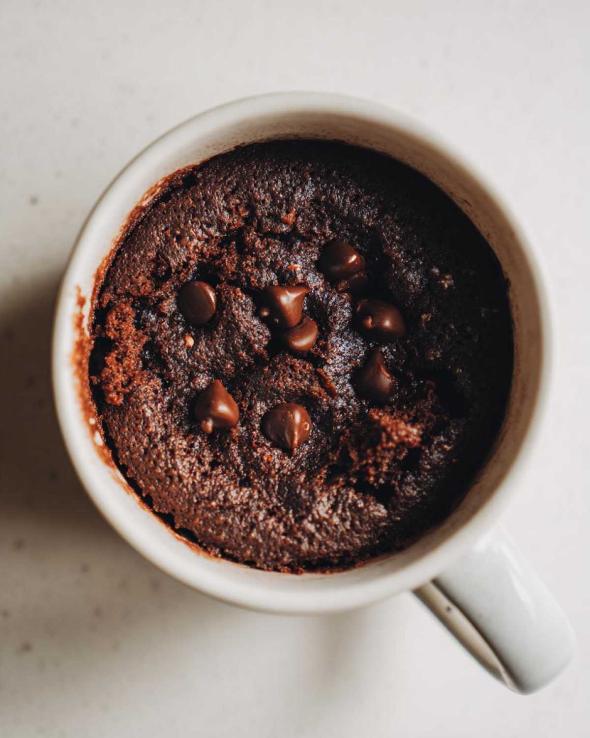 Overhead view of a rich, fudgy chocolate mug cake topped with melted chocolate chips.