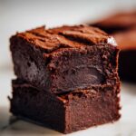 Close-up of two stacked, rich, dark, and fudgy sweet potato brownies resting on a white marble surface.