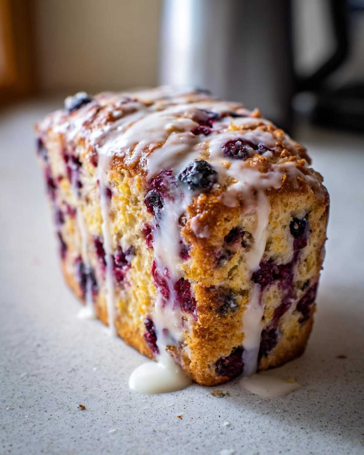 Close-up of a loaf of baked blueberry scones drizzled heavily with white vanilla glaze.