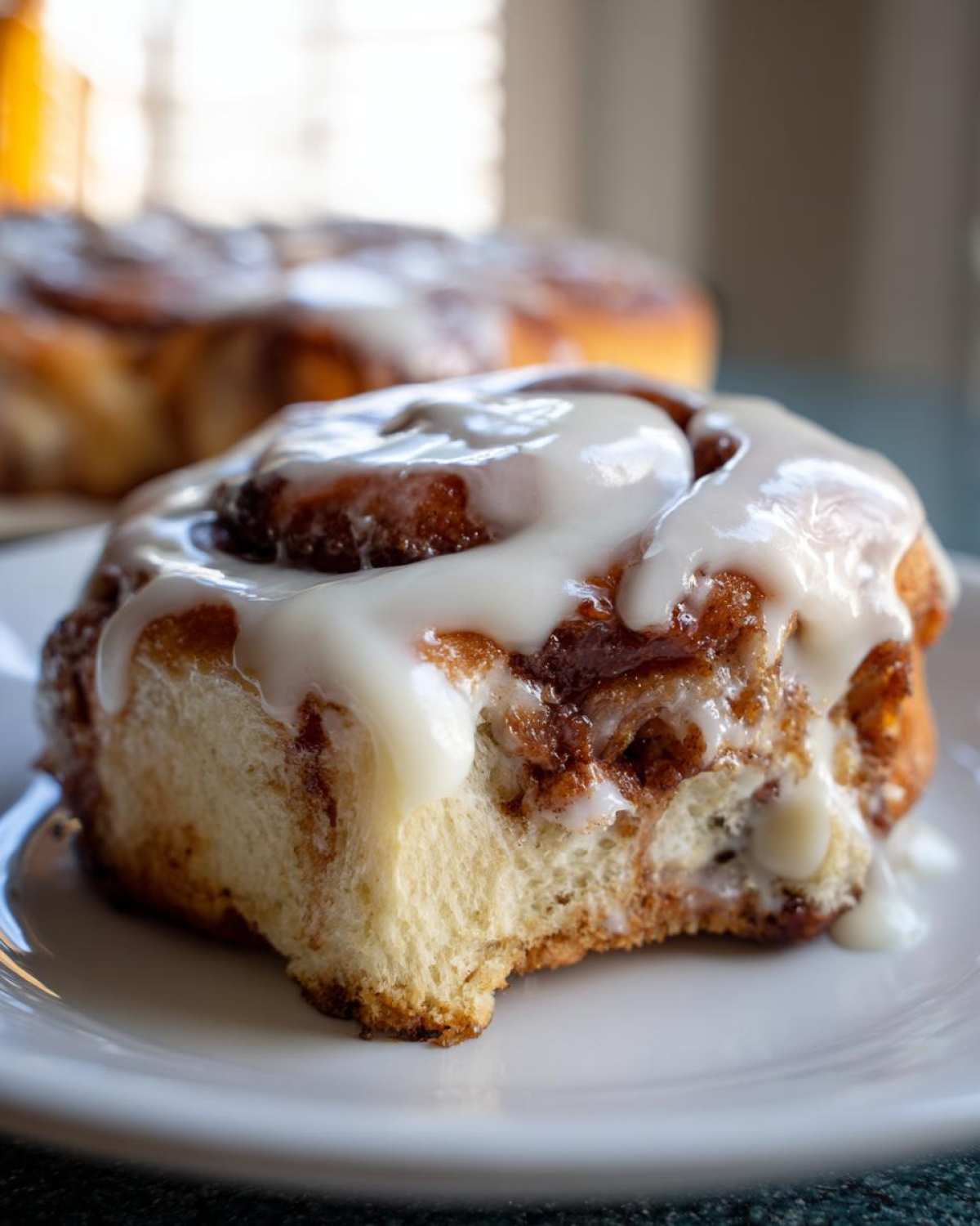 A close-up of a soft, fluffy cinnamon roll topped with thick white icing, with a small bite taken out.
