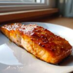 Close-up of a perfectly cooked salmon fillet with a shiny, dark orange glaze on a white plate.