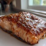 Close-up of a perfectly cooked salmon fillet glazed with a sticky, brown sauce topped with minced garlic.