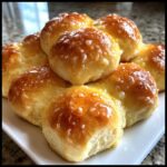 A cluster of freshly baked, golden brown dinner rolls brushed with a shiny glaze and coarse salt.