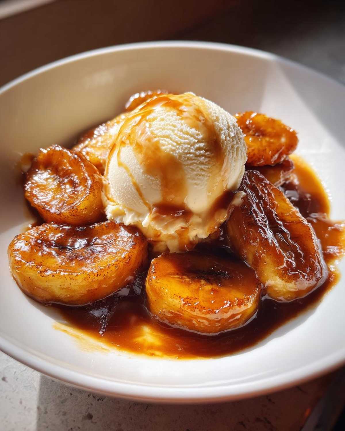 A close-up of Bananas Foster featuring caramelized banana slices swimming in rich sauce, topped with a scoop of vanilla ice cream.