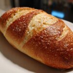 Close-up of a perfectly baked Italian bread loaf with a golden-brown, scored crust sprinkled with coarse salt.