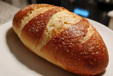 Close-up of a perfectly baked Italian bread loaf with a golden-brown, scored crust sprinkled with coarse salt.