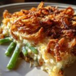 A close-up, appetizing slice of green bean casserole topped with crispy fried onions.