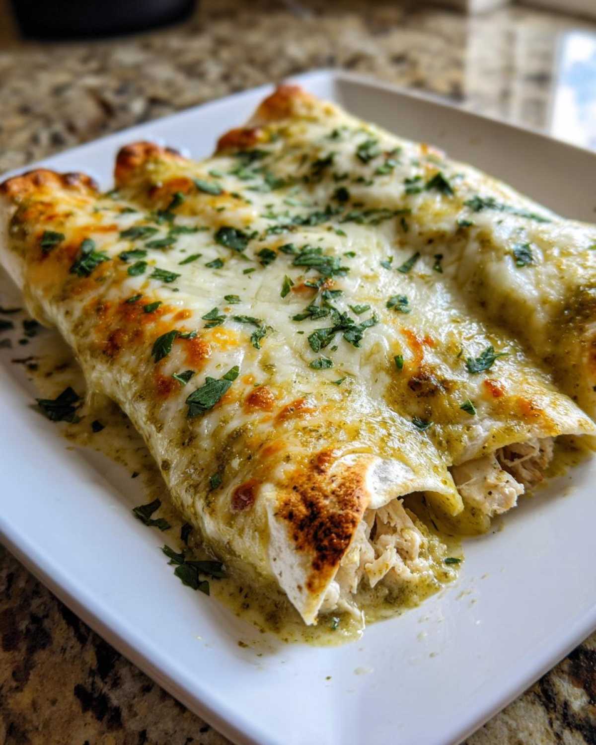 Close-up of three baked green chile chicken enchiladas covered in melted cheese and parsley.