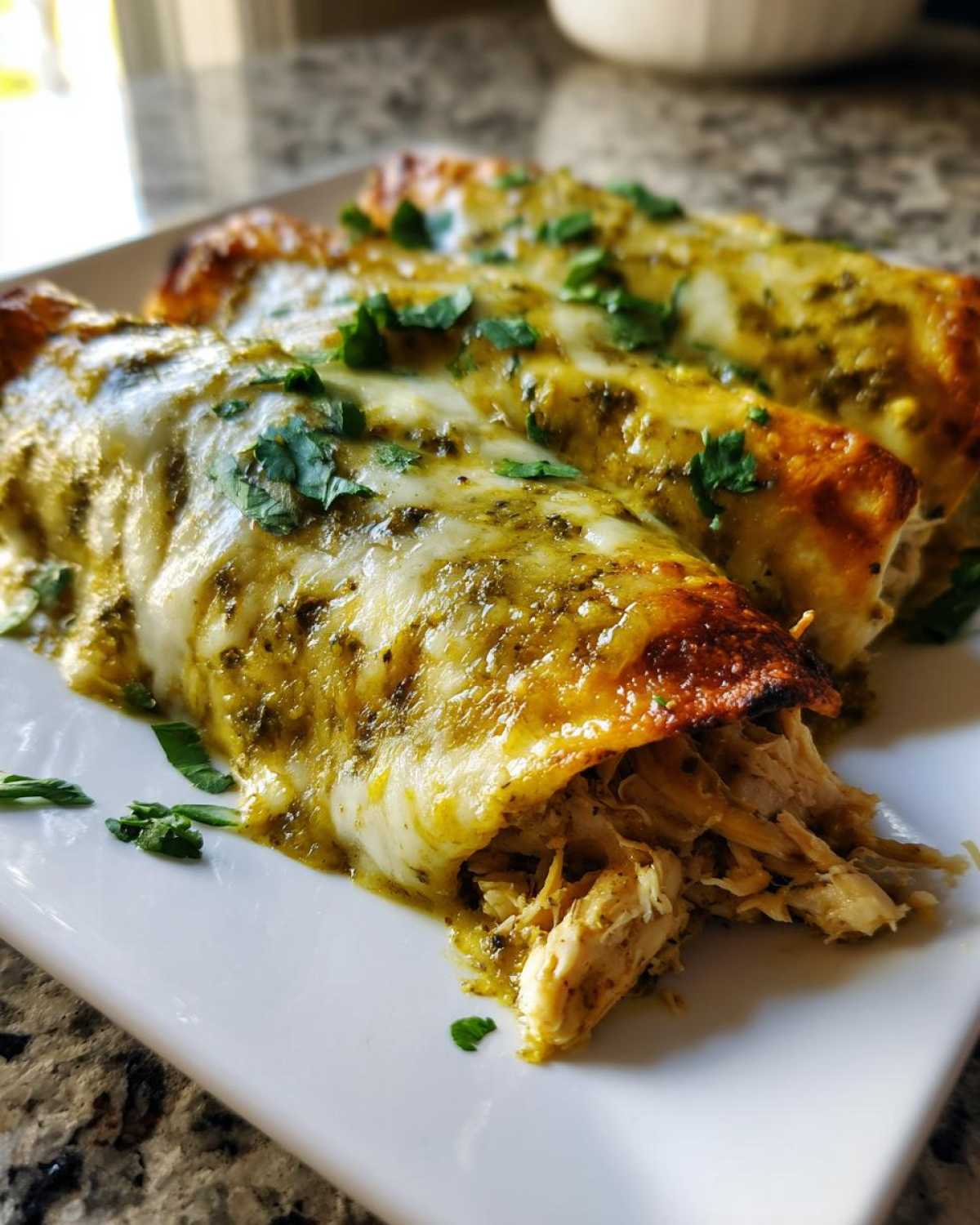 Close-up of three baked green chile chicken enchiladas covered in melted cheese and cilantro.