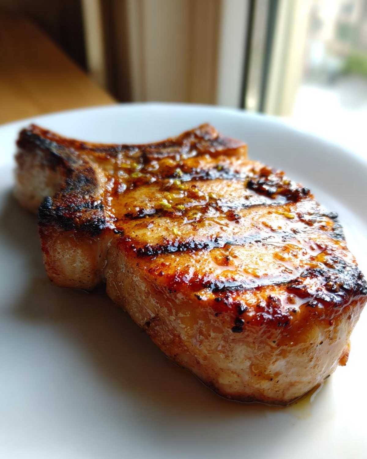 Close-up of a thick, juicy, grilled pork chop showing char marks and a shiny glaze, perfect for a marinade for pork chops.