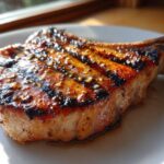 Close-up of a perfectly grilled, thick-cut pork chop showing char marks and a glossy glaze, ideal for a marinade for pork chops.