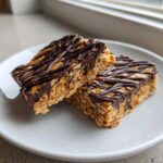 Two stacked, chewy homemade protein bars made with oats and drizzled generously with dark chocolate.