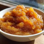Close-up of chunky, spiced homemade applesauce in a small white bowl, glistening in the sunlight.