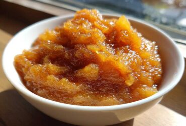 Close-up of chunky, spiced homemade applesauce in a small white bowl, glistening in the sunlight.