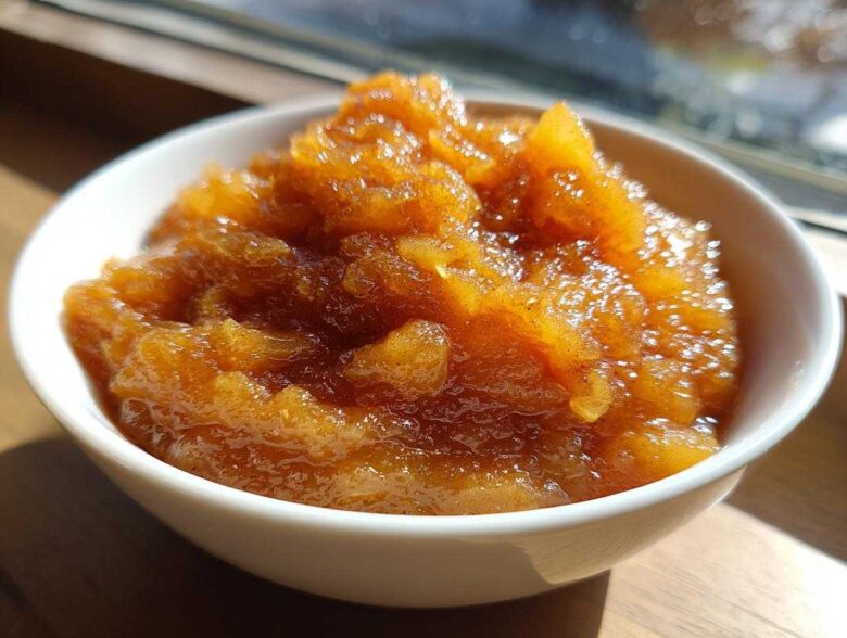 Close-up of chunky, spiced homemade applesauce in a small white bowl, glistening in the sunlight.