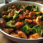 Close-up of glistening, saucy chicken and broccoli pieces cooked together in a white skillet.