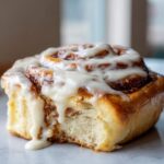A close-up shot of a fluffy, freshly baked cinnamon roll dripping with thick white icing.