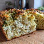 Close-up of a loaf of Italian herb and cheese bread sliced open, showing the fluffy interior and cheesy, herby topping.