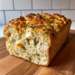 Close-up of a freshly baked Italian herb and cheese bread loaf showing a soft, airy interior and a golden, cheesy, herbed crust.