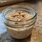 Close-up of apple cinnamon overnight oats prepared in a small glass jar, topped with nuts and cinnamon.