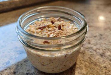 Close-up of apple cinnamon overnight oats prepared in a small glass jar, topped with nuts and cinnamon.