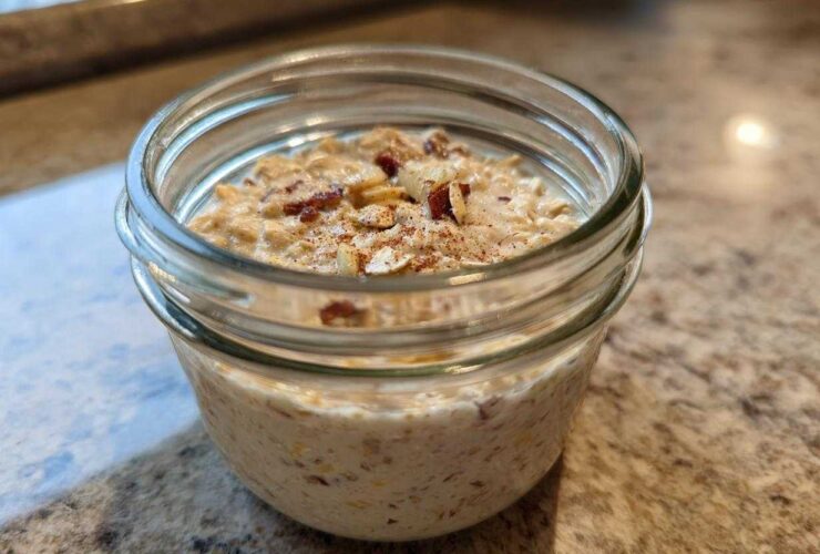Close-up of apple cinnamon overnight oats prepared in a small glass jar, topped with nuts and cinnamon.