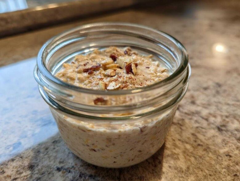 Close-up of apple cinnamon overnight oats prepared in a small glass jar, topped with nuts and cinnamon.