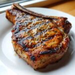Close-up of a perfectly grilled, juicy bone-in pork chop seasoned with herbs, showing char marks from the marinade for pork chops.