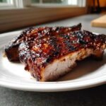 Close-up of a juicy pork steak recipe cut in half, showing a caramelized, dark glaze and tender interior.
