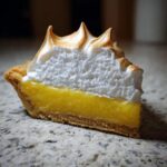 Close-up of a slice of lemon meringue pie showing bright yellow filling and tall, toasted meringue peaks.